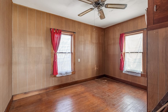 spare room featuring wood-type flooring, ceiling fan, and wooden walls