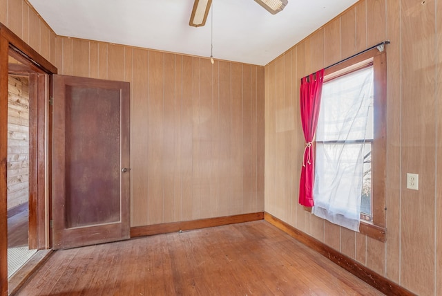 unfurnished room with ceiling fan, light hardwood / wood-style floors, and wood walls