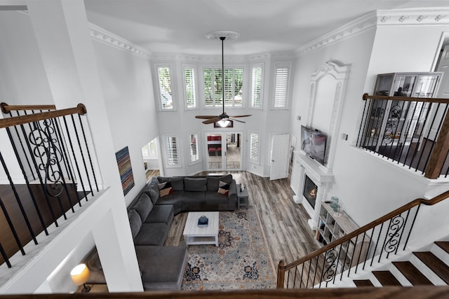 living room with ceiling fan, ornamental molding, wood-type flooring, and a high ceiling