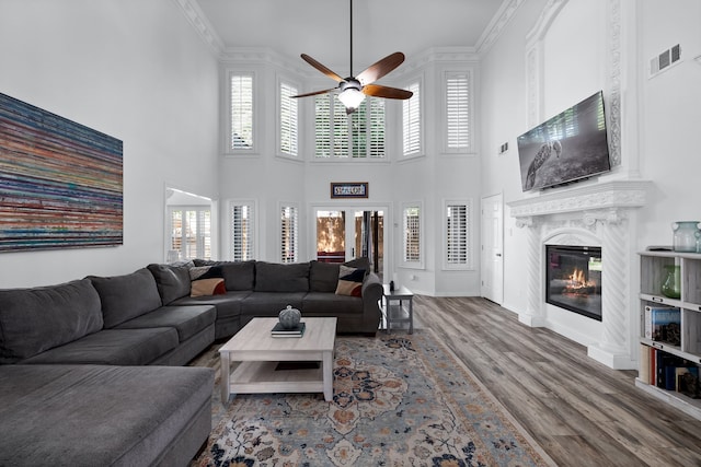 living room with crown molding, ceiling fan, hardwood / wood-style floors, a high ceiling, and a fireplace