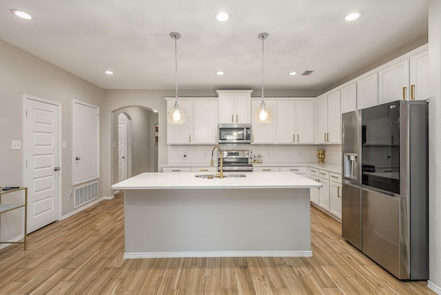 kitchen with sink, a kitchen island with sink, hanging light fixtures, stainless steel appliances, and white cabinets