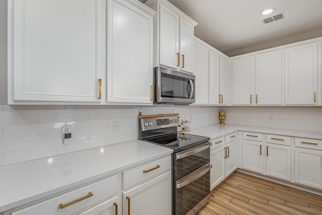 kitchen featuring tasteful backsplash, stainless steel appliances, light hardwood / wood-style floors, and white cabinets