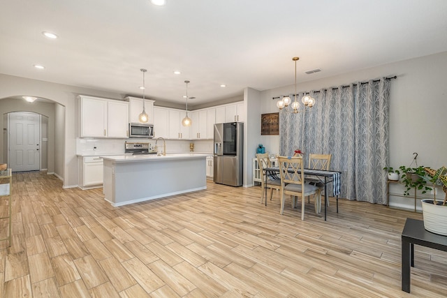 kitchen featuring sink, white cabinetry, a kitchen island with sink, stainless steel appliances, and decorative light fixtures