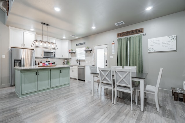 kitchen with appliances with stainless steel finishes, white cabinetry, hanging light fixtures, backsplash, and a kitchen island