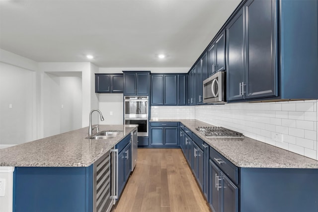 kitchen with blue cabinetry, sink, appliances with stainless steel finishes, hardwood / wood-style floors, and a kitchen island with sink