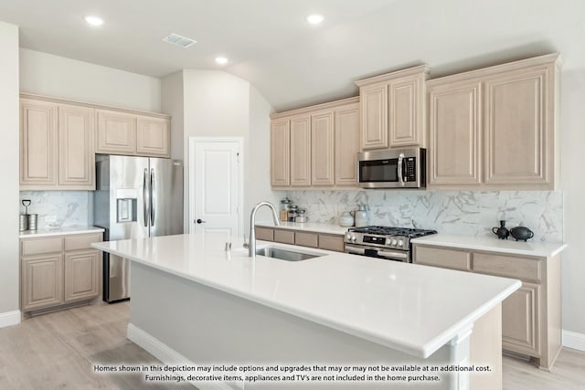 kitchen featuring sink, appliances with stainless steel finishes, a kitchen island with sink, decorative backsplash, and vaulted ceiling