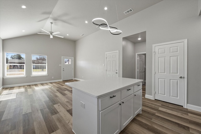 kitchen with dark wood-type flooring, ceiling fan, high vaulted ceiling, white cabinets, and a kitchen island