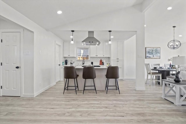 kitchen with pendant lighting, white cabinets, vaulted ceiling, and wall chimney exhaust hood