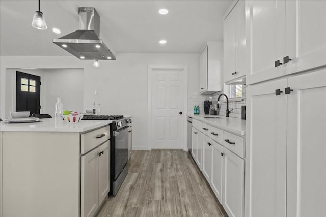 kitchen with pendant lighting, sink, stainless steel gas range oven, white cabinets, and island exhaust hood