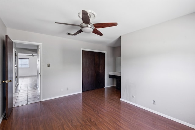 unfurnished bedroom with ceiling fan, dark wood-type flooring, a closet, and baseboards