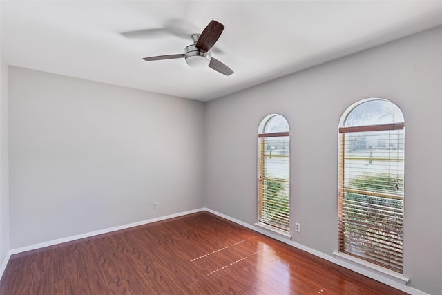 unfurnished room with dark wood-style flooring, a ceiling fan, and baseboards