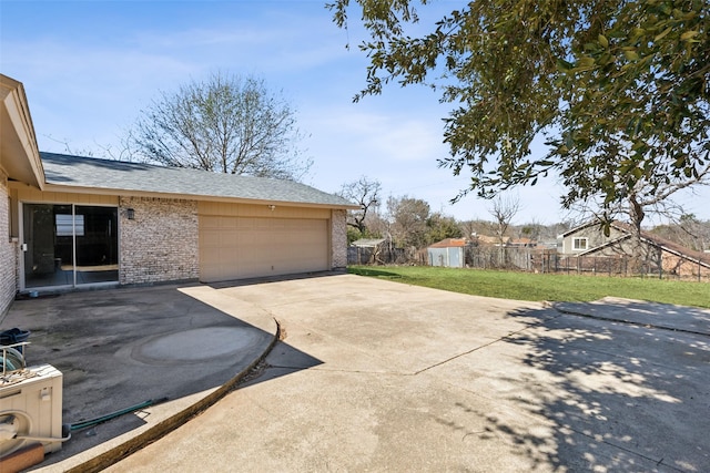 view of home's exterior featuring brick siding, concrete driveway, a lawn, an attached garage, and fence