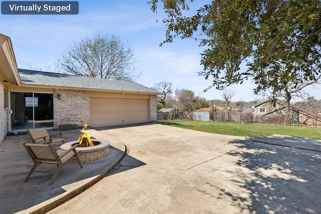 view of patio featuring an attached garage, an outdoor fire pit, fence, and concrete driveway