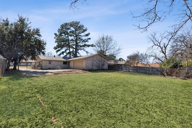 view of yard featuring a garage, a fenced backyard, and concrete driveway