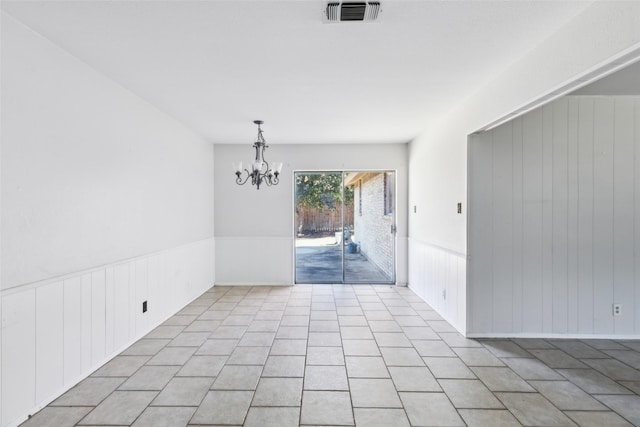 unfurnished dining area with a chandelier, light tile patterned floors, a wainscoted wall, and visible vents