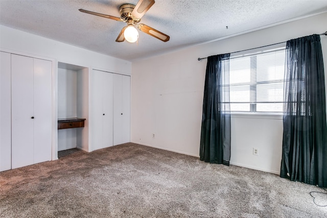 unfurnished bedroom with two closets, a textured ceiling, ceiling fan, and carpet