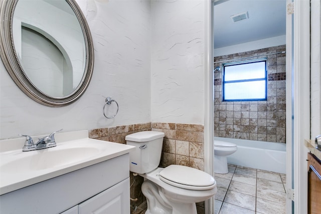 full bathroom with tile walls, tiled shower / bath combo, vanity, tile patterned flooring, and toilet