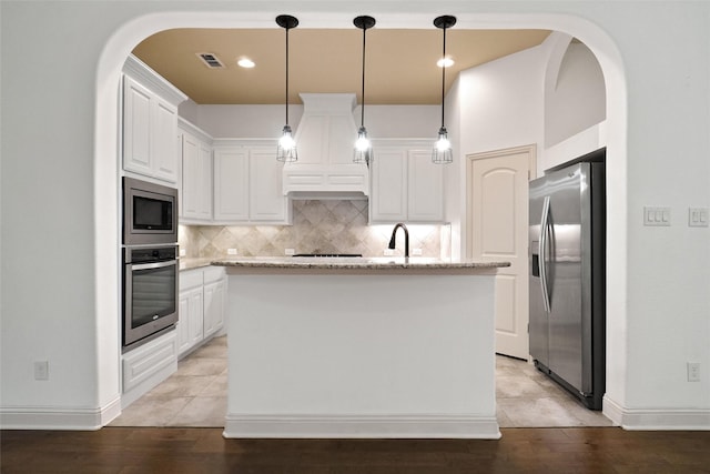 kitchen featuring tasteful backsplash, hanging light fixtures, stainless steel appliances, a kitchen island with sink, and white cabinets