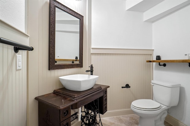 bathroom featuring tile patterned flooring, sink, wooden walls, and toilet