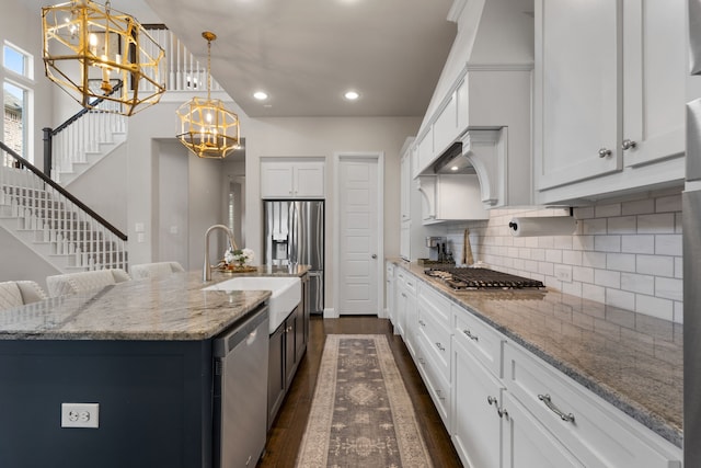 kitchen with white cabinetry, an inviting chandelier, decorative light fixtures, appliances with stainless steel finishes, and a kitchen island with sink