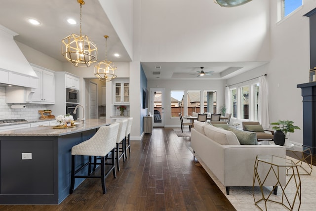 living room featuring a tray ceiling, ceiling fan with notable chandelier, and dark hardwood / wood-style floors