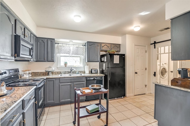 kitchen featuring sink, light tile patterned floors, independent washer and dryer, a barn door, and black appliances