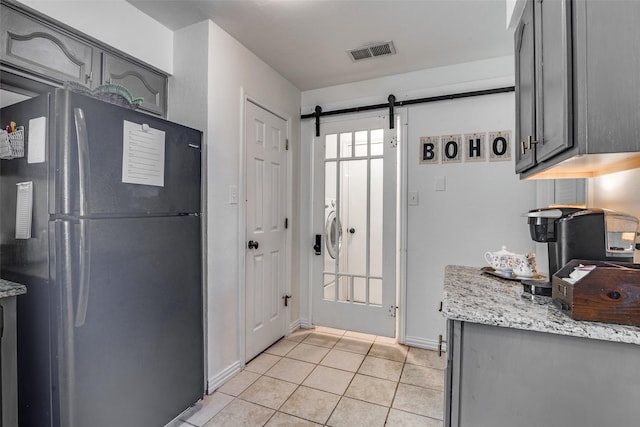 kitchen with light tile patterned floors, gray cabinets, a barn door, and black fridge