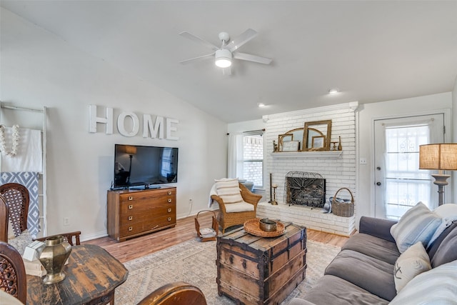 living room featuring vaulted ceiling, plenty of natural light, light hardwood / wood-style floors, and a brick fireplace