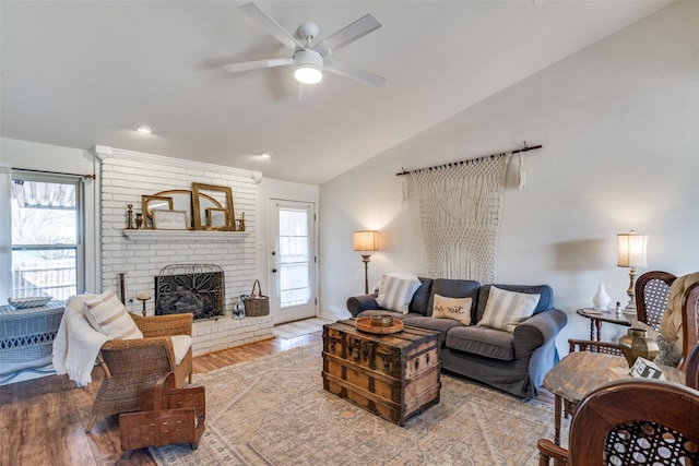 living room with ceiling fan, lofted ceiling, light wood-type flooring, and a brick fireplace