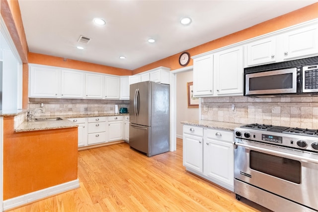 kitchen with tasteful backsplash, white cabinetry, sink, stainless steel appliances, and light wood-type flooring