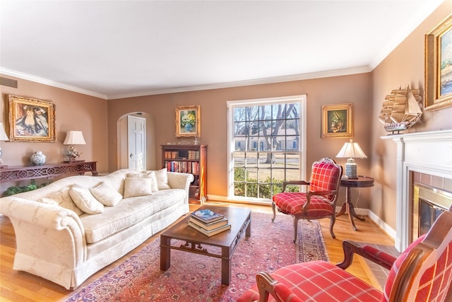 living room featuring a tile fireplace, crown molding, and light hardwood / wood-style flooring