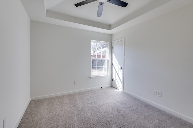 empty room featuring ceiling fan, a raised ceiling, and light carpet