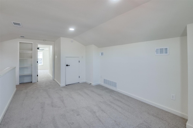 additional living space with light carpet, built in shelves, and vaulted ceiling