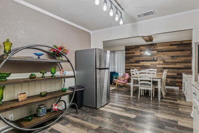 kitchen featuring crown molding, stainless steel refrigerator, white cabinets, and wood walls