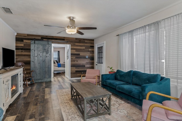 living room featuring a barn door, dark hardwood / wood-style floors, wooden walls, and ceiling fan