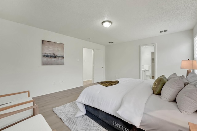 bedroom with ensuite bath, hardwood / wood-style floors, and a textured ceiling