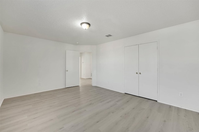 unfurnished bedroom with a textured ceiling, light wood-type flooring, and a closet