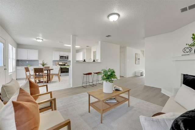 living room featuring light wood-type flooring, a textured ceiling, and a fireplace