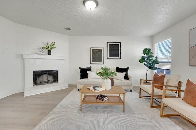 living room with a brick fireplace, a textured ceiling, and light hardwood / wood-style flooring