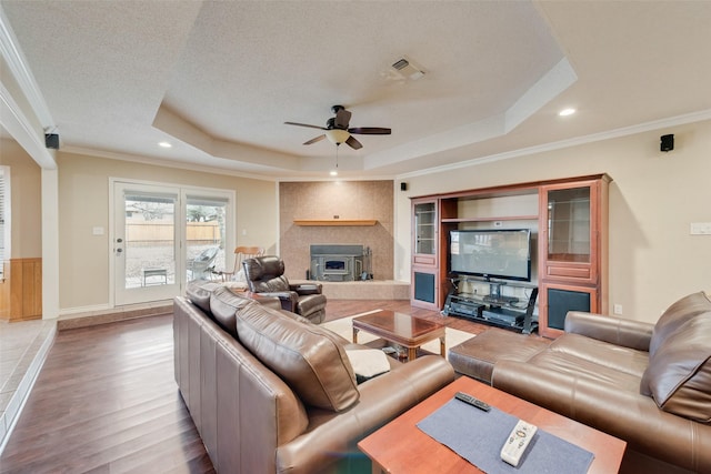 living room with ornamental molding, ceiling fan, a tray ceiling, a textured ceiling, and light hardwood / wood-style flooring