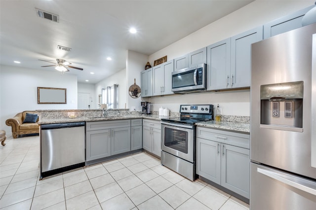 kitchen with sink, light tile patterned floors, appliances with stainless steel finishes, light stone counters, and kitchen peninsula