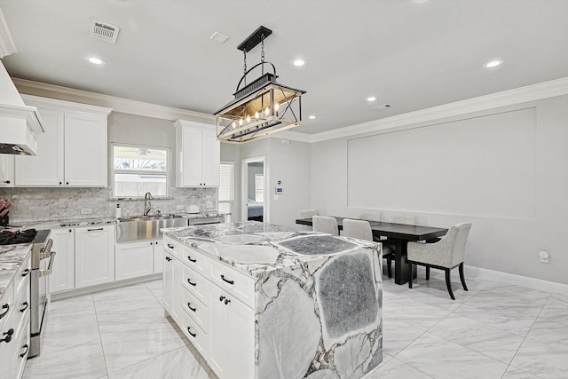 kitchen with light stone counters, stainless steel range, ornamental molding, a kitchen island, and white cabinets