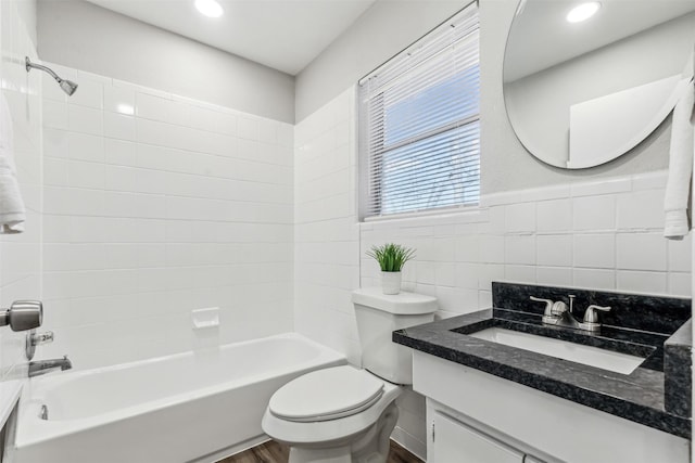 full bathroom with tiled shower / bath, hardwood / wood-style floors, tile walls, vanity, and toilet