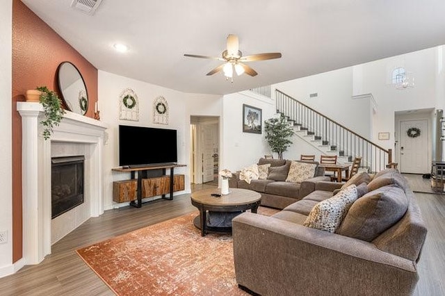 living room featuring a tiled fireplace, wood-type flooring, and ceiling fan