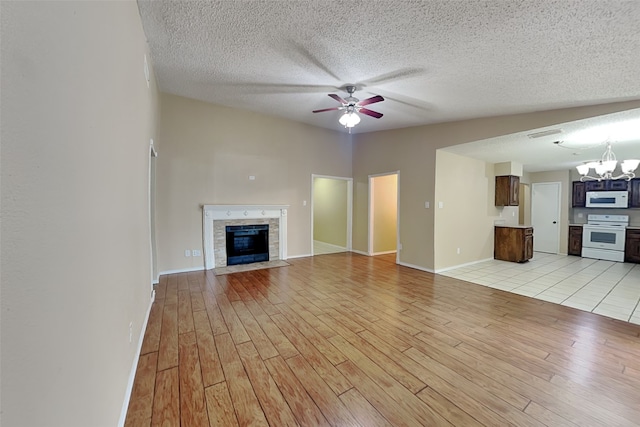 unfurnished living room featuring lofted ceiling, ceiling fan with notable chandelier, a textured ceiling, and light wood-type flooring