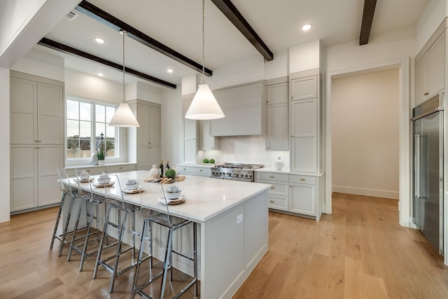 kitchen featuring pendant lighting, premium appliances, a large island, light hardwood / wood-style floors, and beam ceiling