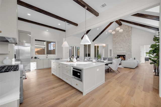 kitchen featuring appliances with stainless steel finishes, a kitchen island with sink, hanging light fixtures, white cabinets, and beamed ceiling