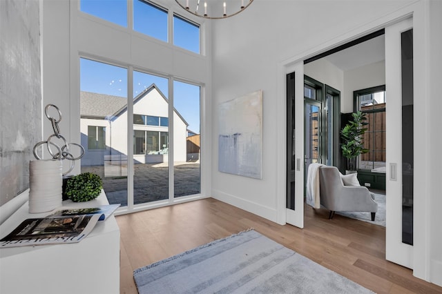 entryway with baseboards, wood finished floors, a towering ceiling, and an inviting chandelier