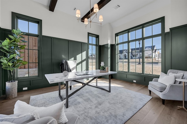 office featuring beam ceiling, a notable chandelier, visible vents, a decorative wall, and wood finished floors