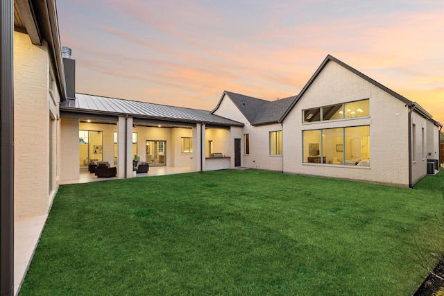 back house at dusk featuring an outdoor living space, a yard, central AC, and a patio area